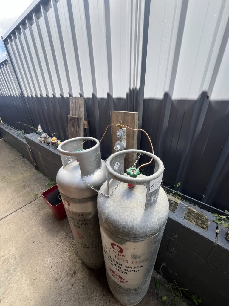 Twin LPG gas cylinders secured to a fence with a changeover regulator