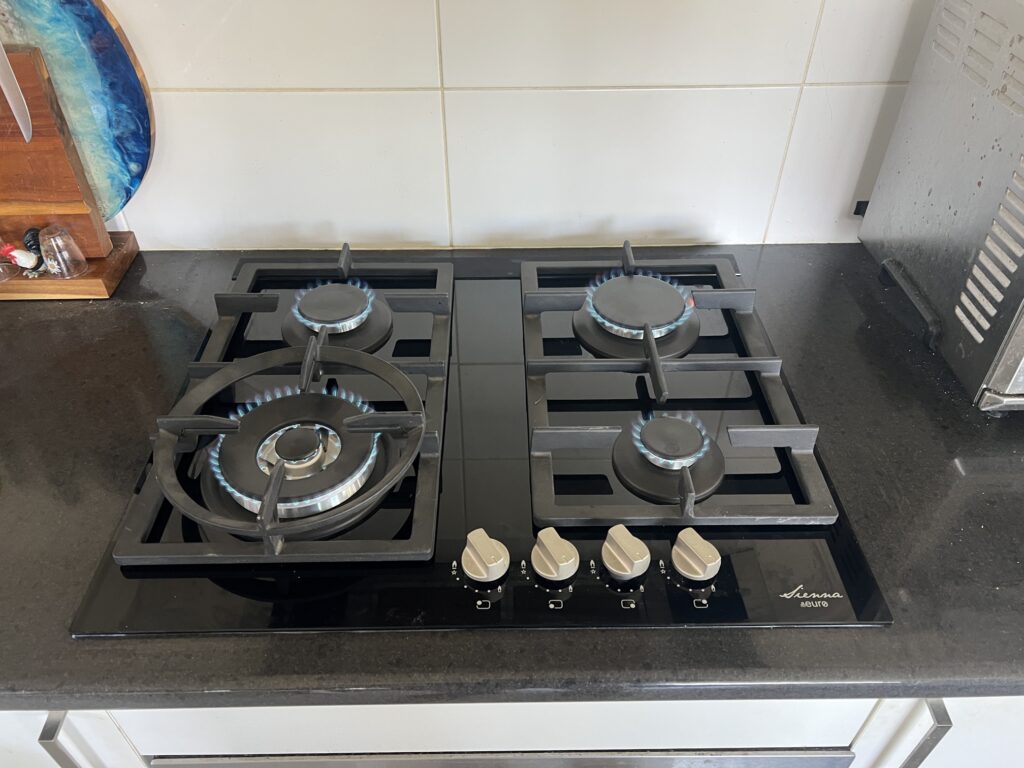 Newly installed four-burner gas cooktop with burners alight on a stone benchtop